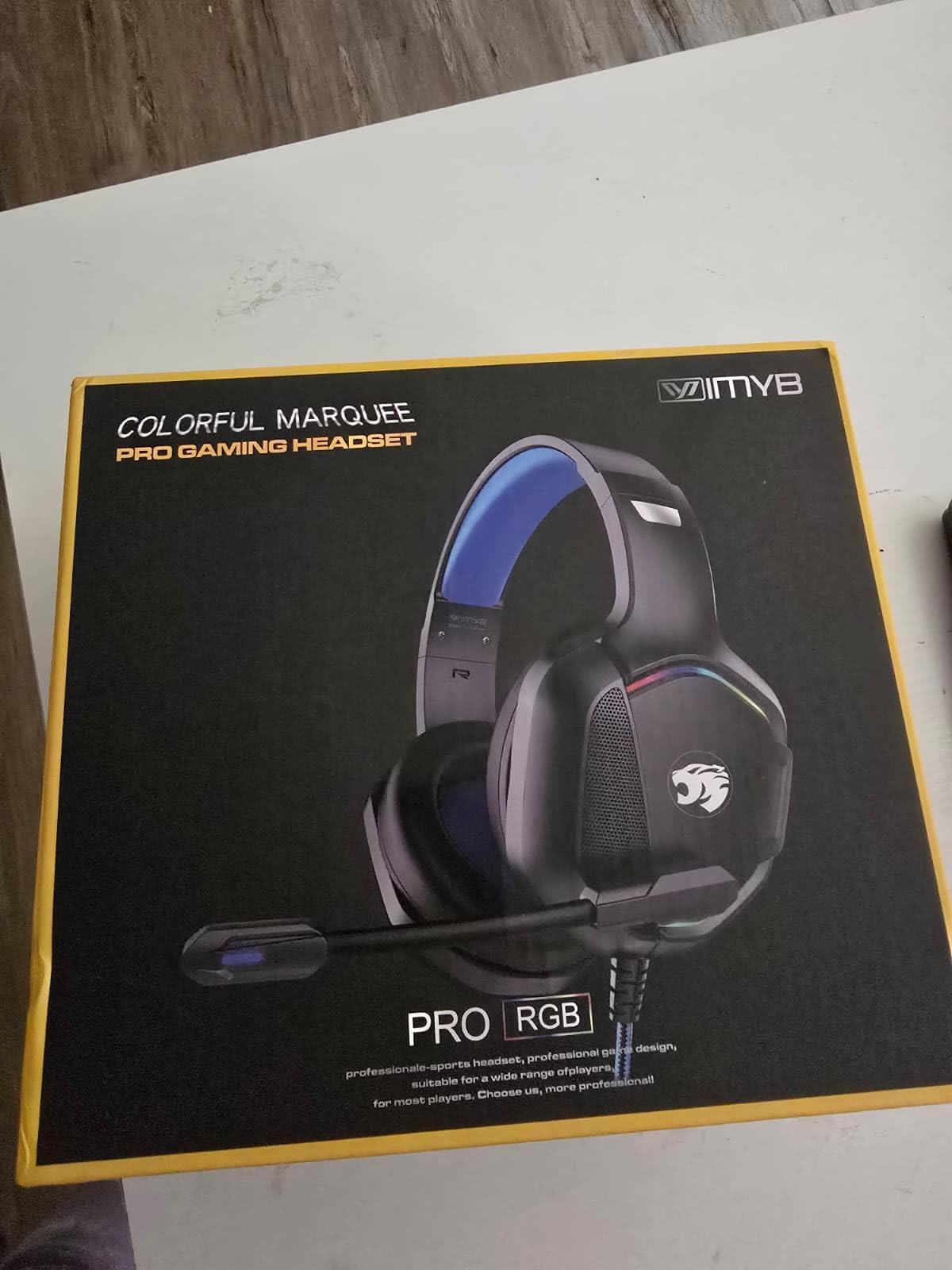 IMYB Colorful Marquee Pro Gaming Headset retail box on a white desk, printed with a blue and black RGB headset