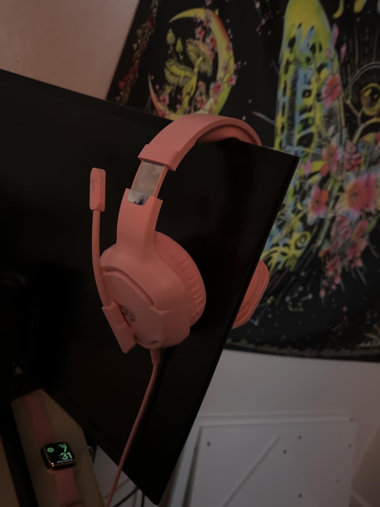 Pink IMYB A36 gaming headset hanging over the top corner of a monitor in a dark room, boom microphone extended