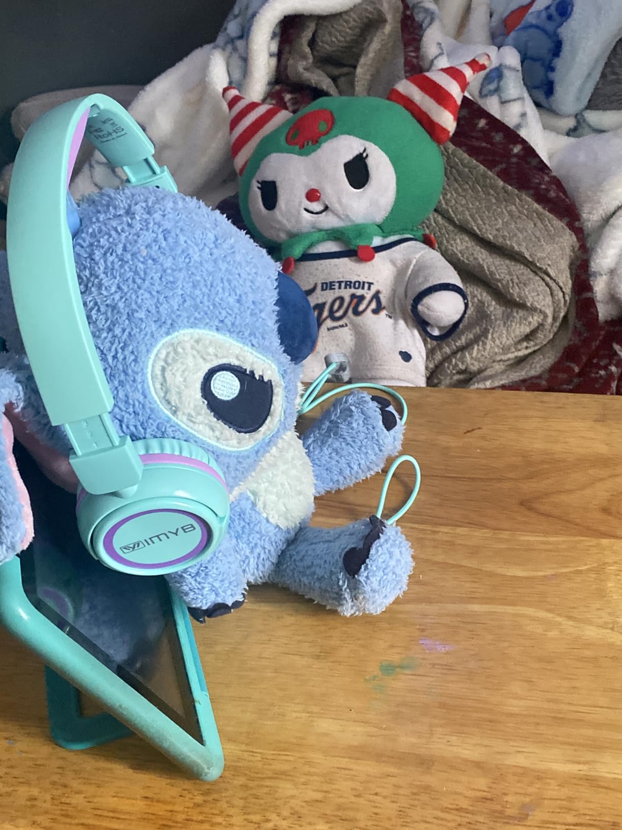Mint green IMYB V1 kids headphones resting against a plush toy beside a tablet in a matching case